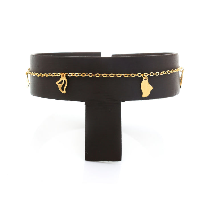 A wide black cuff bracelet with a delicate gold chain and small dangling gold charms, displayed on a black T-stand against a white background.