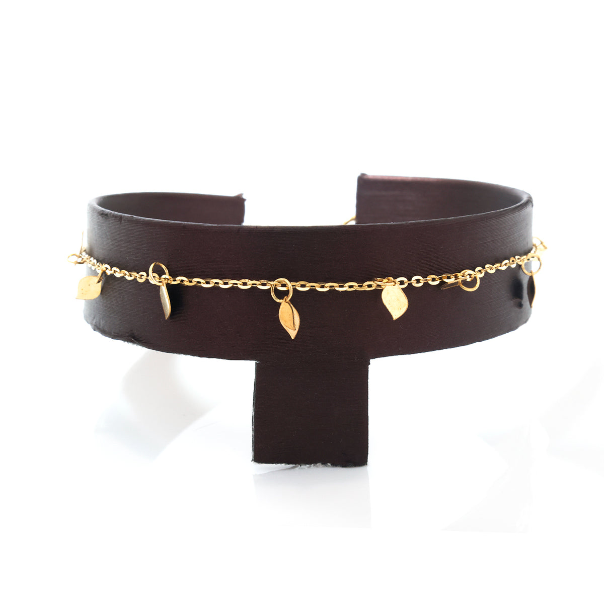 A dark brown leather cuff bracelet with a delicate gold chain and leaf charms draped across the front, displayed on a white background.