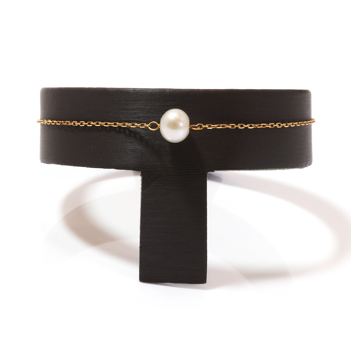 A delicate gold chain bracelet with a single white pearl bead, displayed on a black T-shaped stand against a white background.