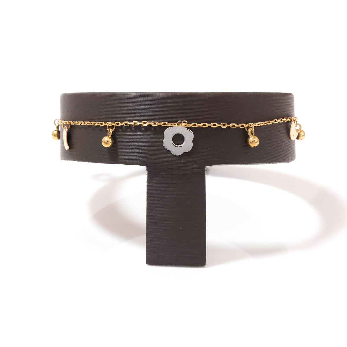 A gold chain bracelet with small dangling gold beads and a central white flower charm, displayed on a black T-shaped stand against a white background.