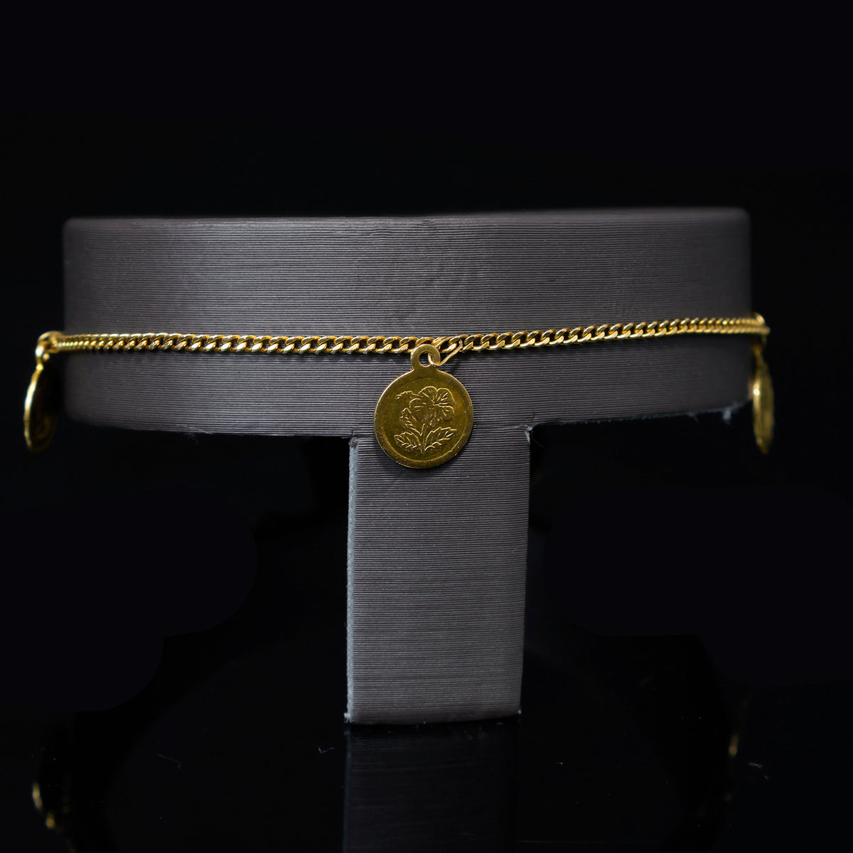 Gold necklace with a circular pendant on a metallic stand against a black background