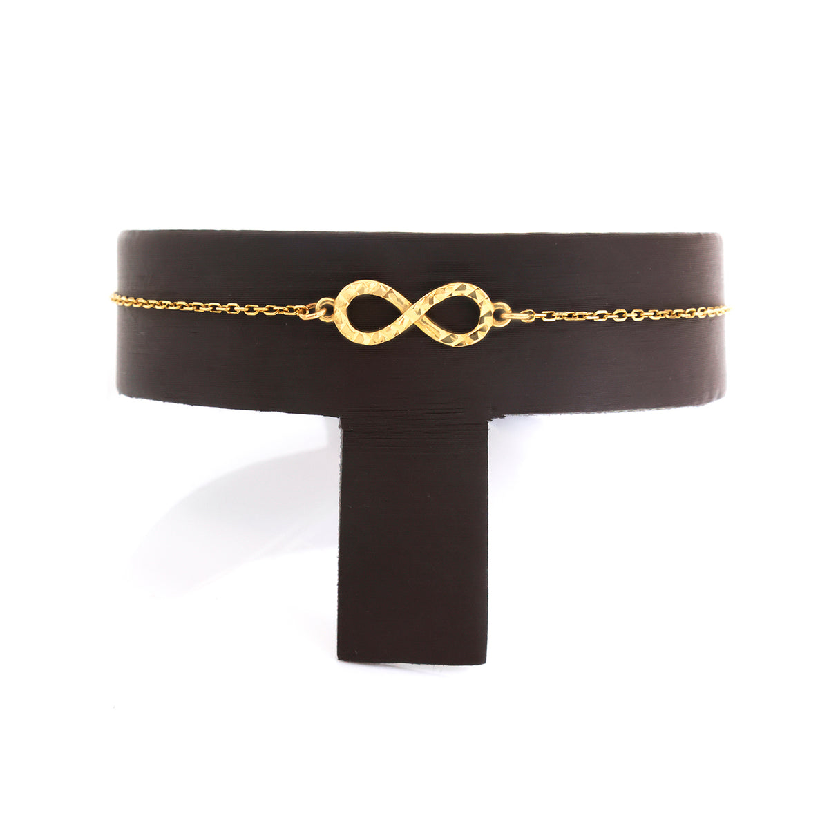 A delicate gold chain bracelet with a textured infinity symbol centerpiece, displayed on a black T-stand against a white background.
