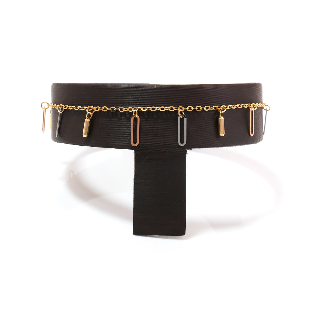 A wide black belt with a thin gold chain running around the waist and several dangling bar-shaped charms in gold, rose gold, and silver, displayed on a black stand against a white background.