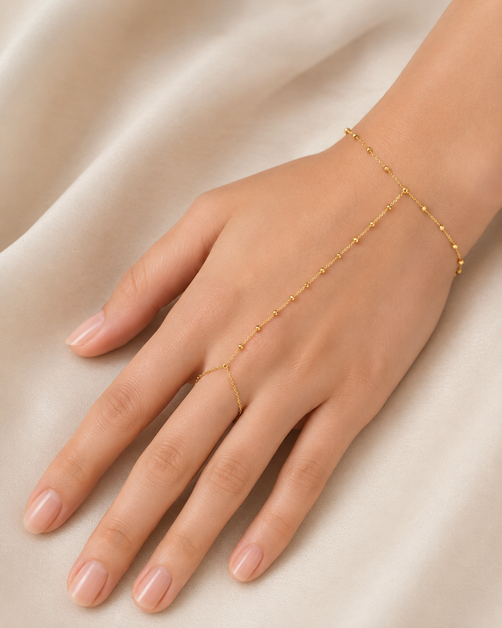 Gold hand chain on a hand against a beige background
