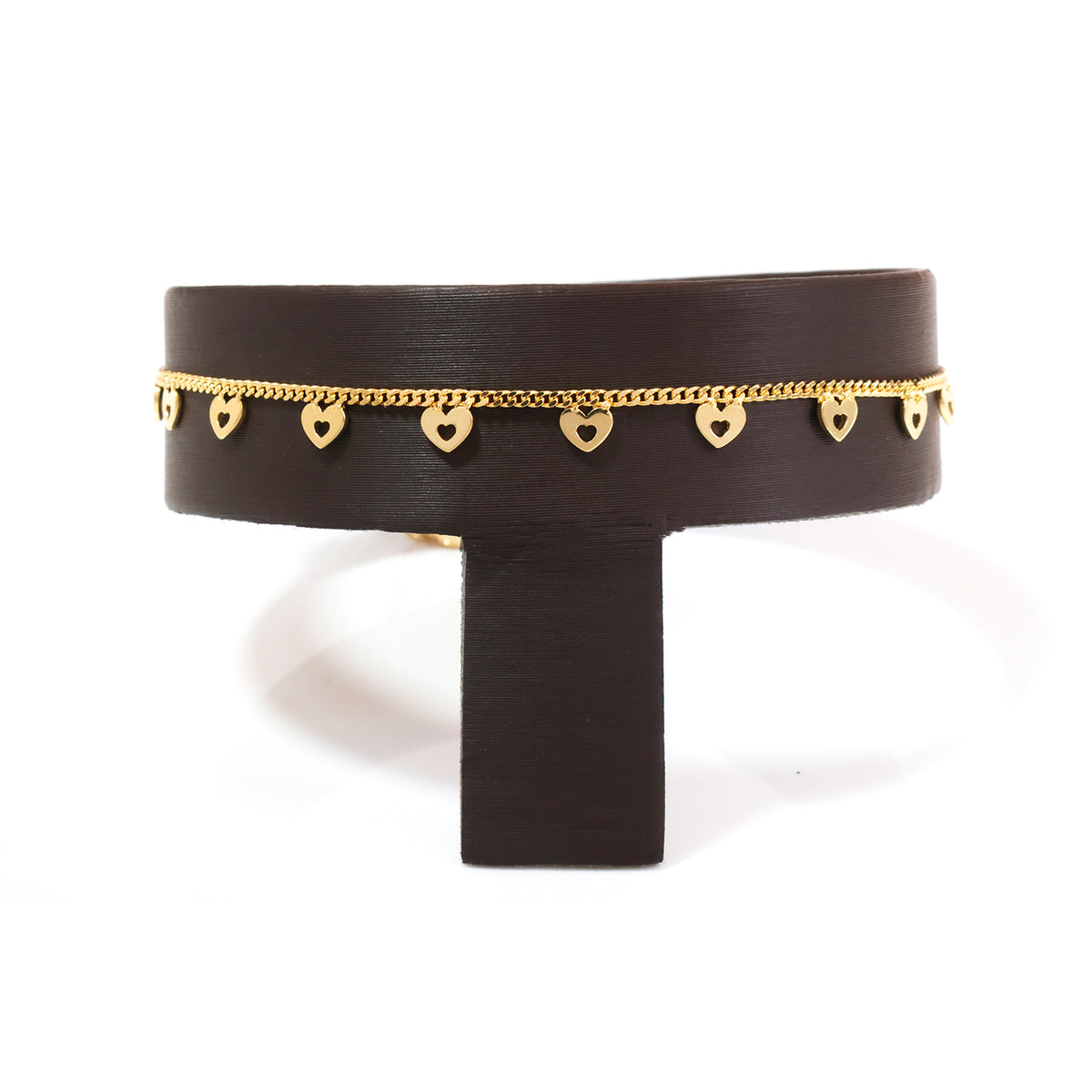 A wide black cuff bracelet with a delicate gold chain running along the top edge and small dangling gold heart charms, displayed on a black stand against a white background.