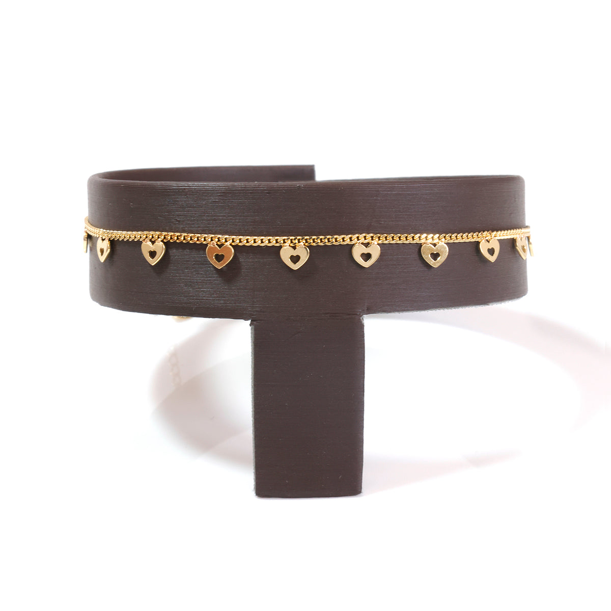 A dark brown cuff bracelet with a delicate gold chain and small heart charms, displayed on a matching dark brown stand against a white background.