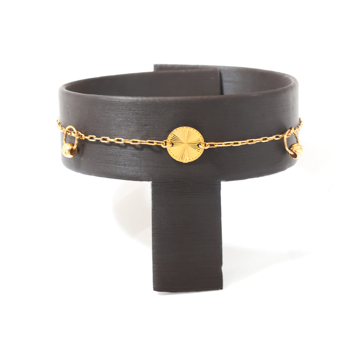 A gold chain bracelet with a round textured disc charm and small dangling beads, displayed on a black T-shaped jewelry stand against a white background.