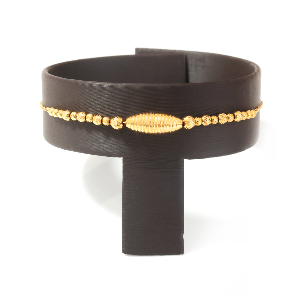 A gold beaded bracelet with a textured central oval bead, displayed on a black stand against a white background.