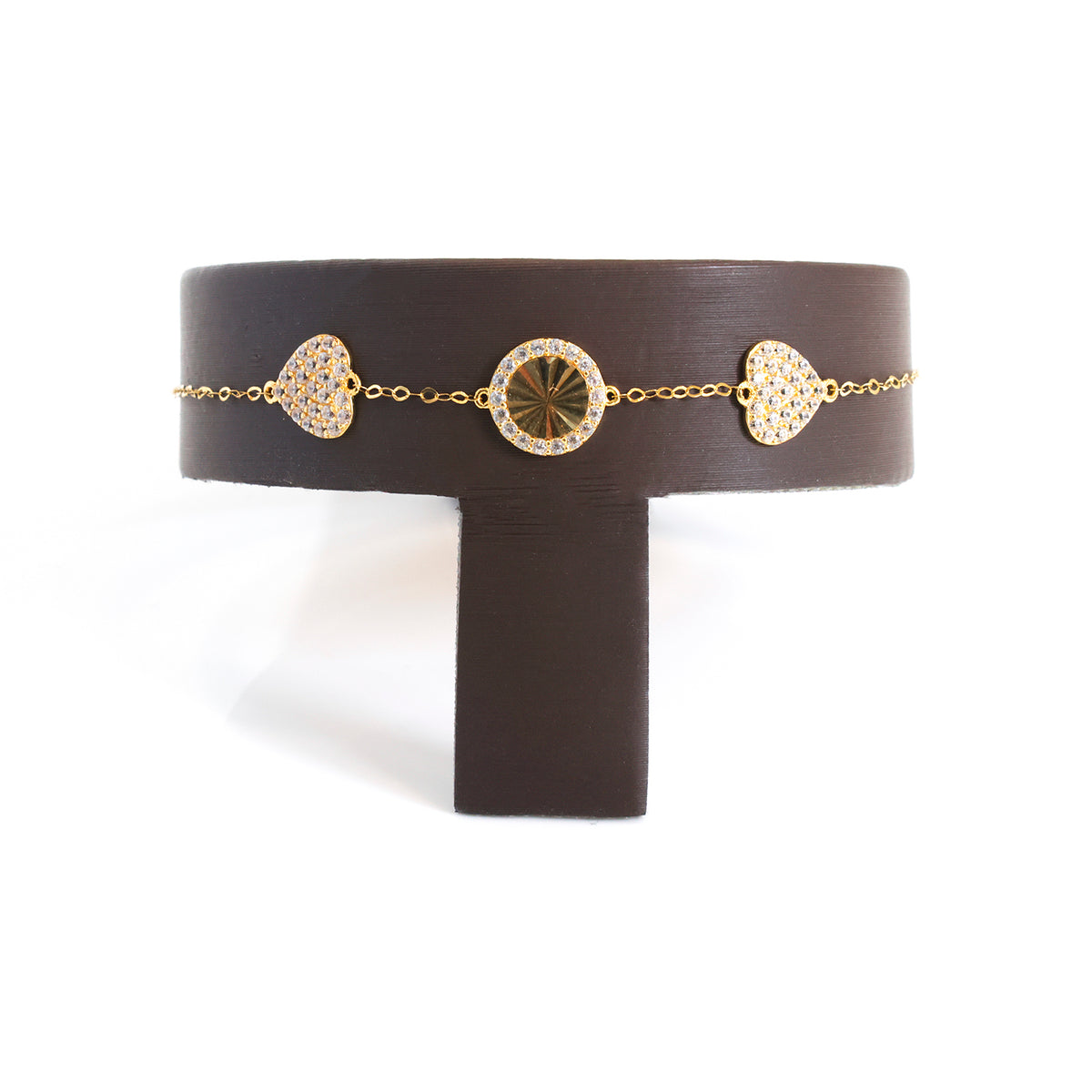 A gold chain bracelet with three heart-shaped pavé medallions, displayed on a dark brown T-stand against a white background.