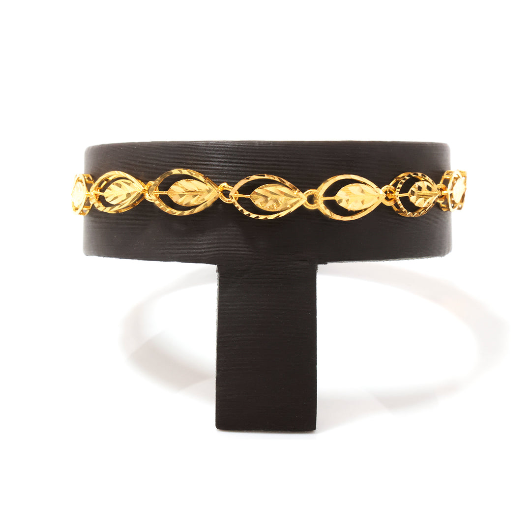 A gold chain bracelet with leaf and oval links, displayed on a black jewelry stand against a white background.