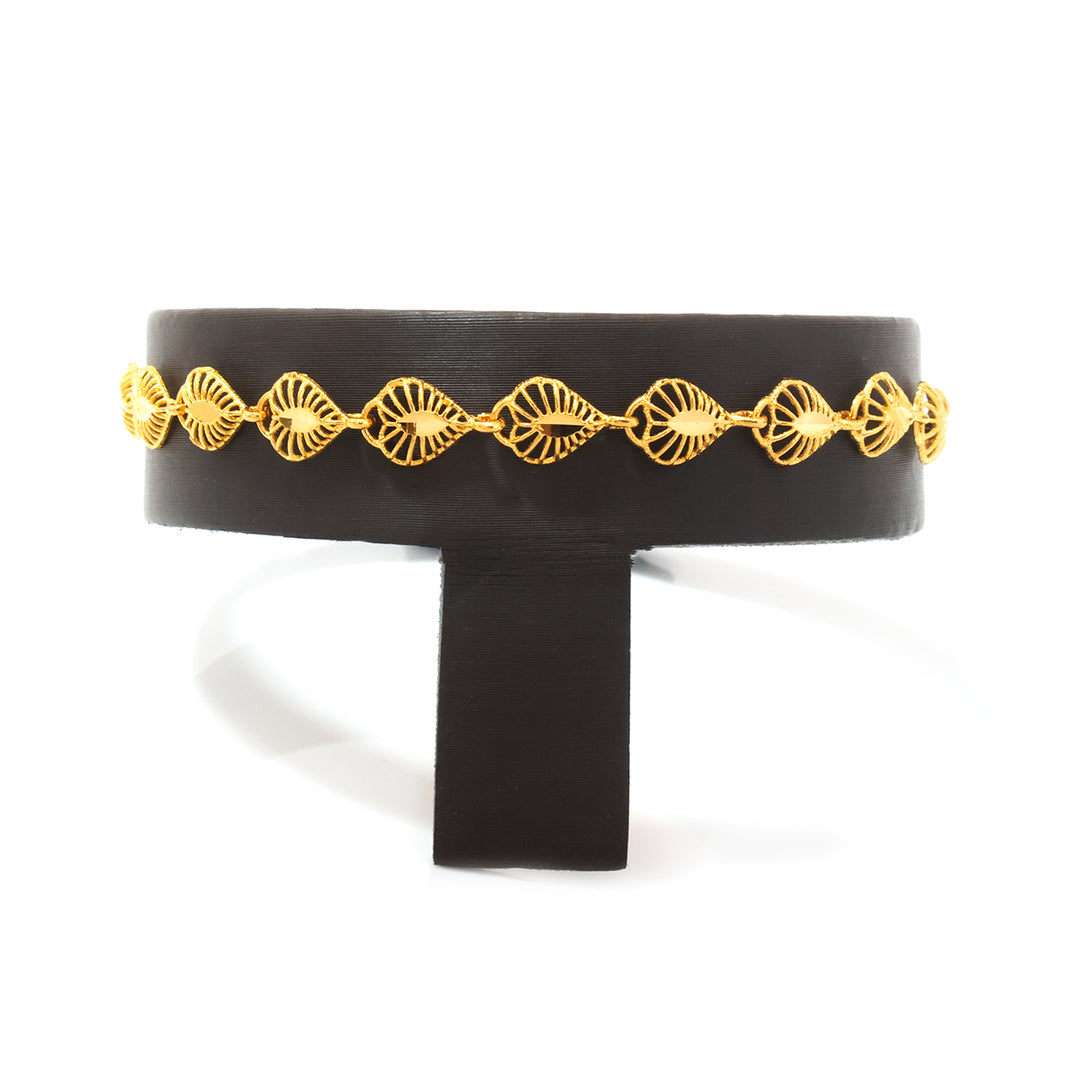 A wide black cuff bracelet with a decorative gold chain of fan-shaped links, displayed on a black stand against a white background.