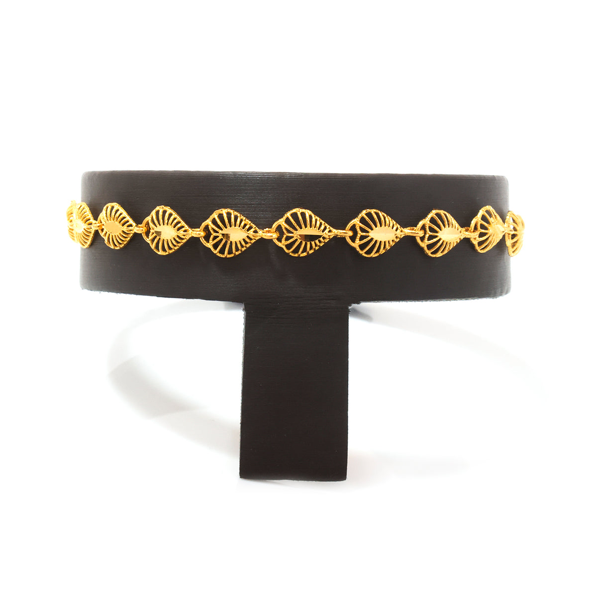 A wide black cuff bracelet with a decorative gold chain of fan-shaped links, displayed on a black stand against a white background.