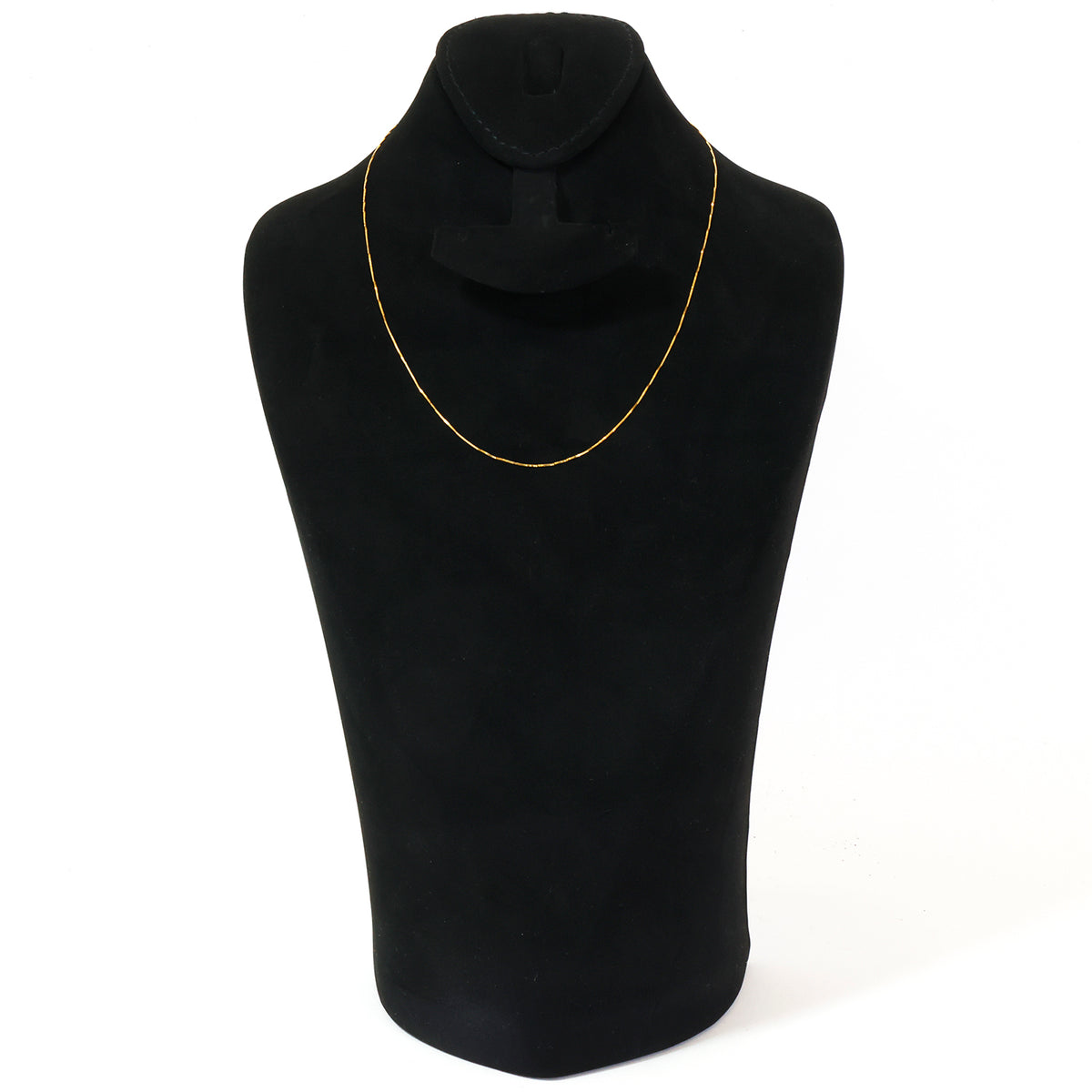 A delicate gold chain necklace displayed on a black velvet jewelry bust against a plain white background.