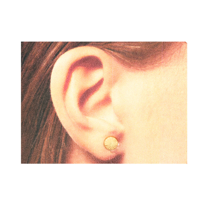 Close-up of an ear wearing a gold earring with a plain background
