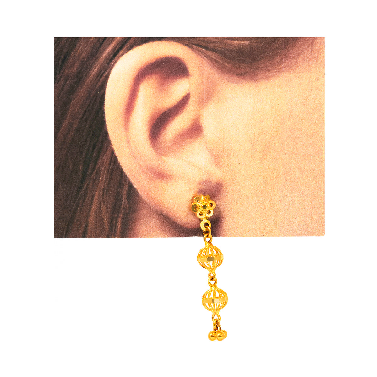Gold earring worn on an ear with a plain background