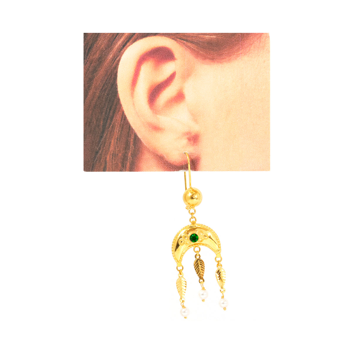 Gold earring with green gemstone worn on an ear, white background