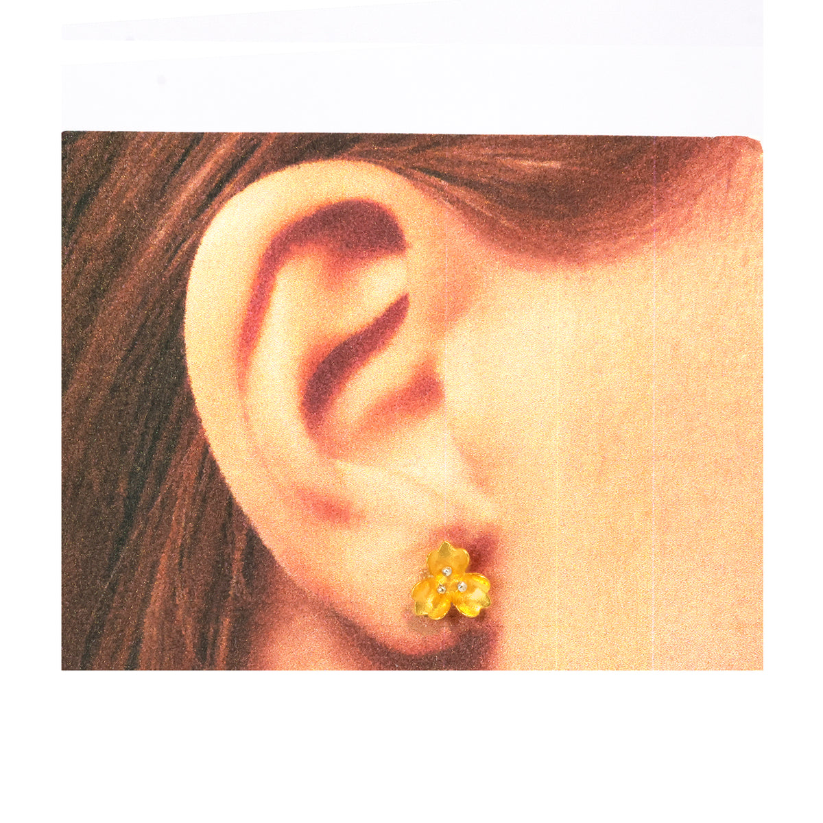 Close-up of an ear wearing a yellow flower-shaped earring on a white background