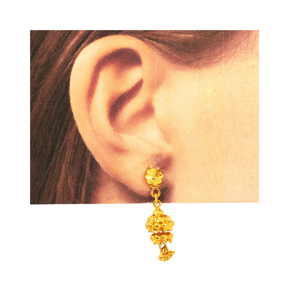 Gold earring worn on an ear with a plain background