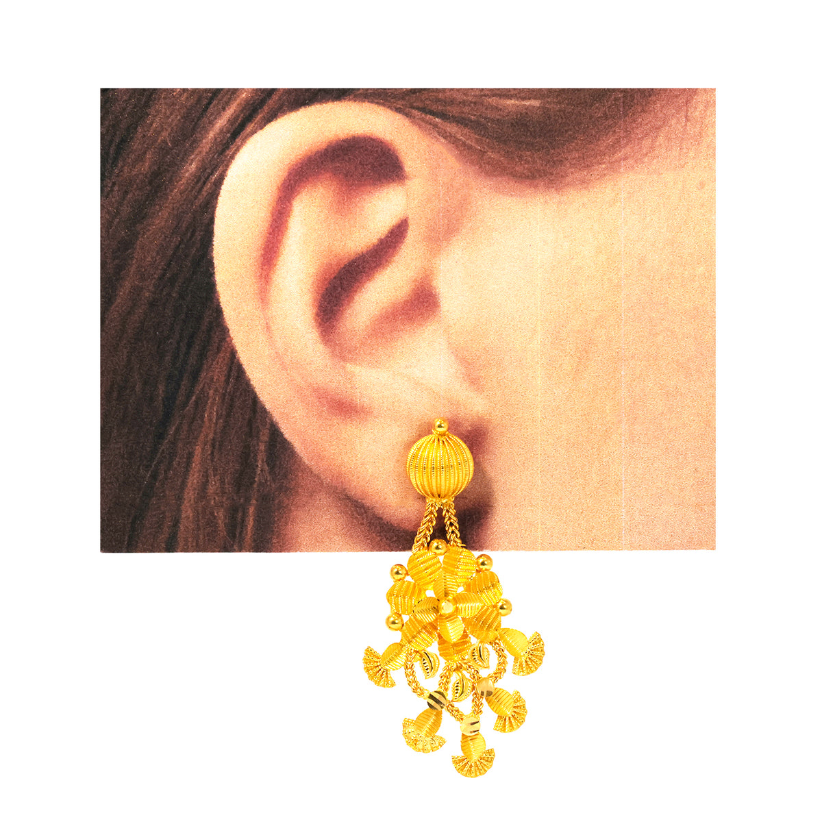 Gold earring worn on an ear with a plain background