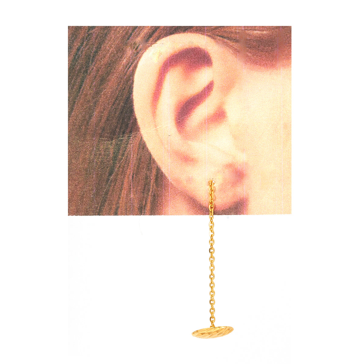 Gold chain earring worn on an ear with a plain background