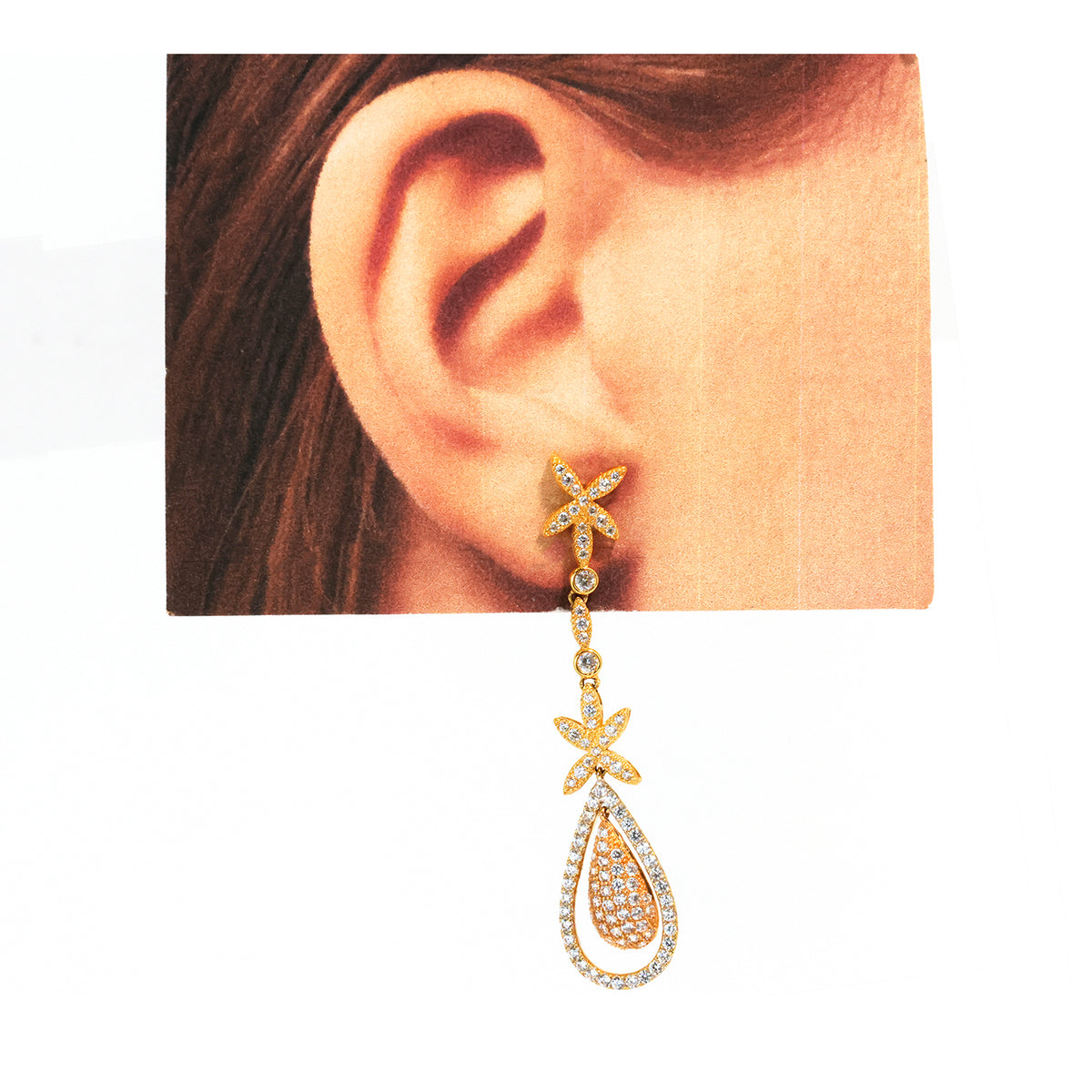 Gold and diamond earring worn by a person with a plain background