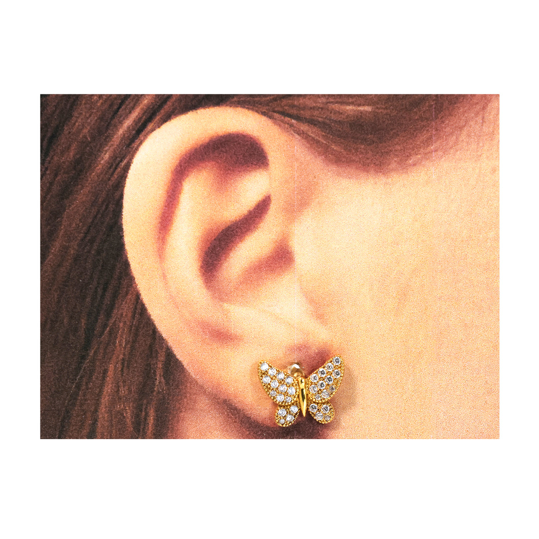 Butterfly-shaped earring worn on an ear with a plain background