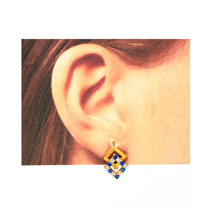 Gold earring with blue and clear stones worn by a person