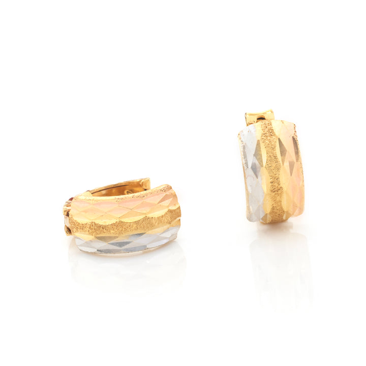 A pair of gold hoop earrings with a textured hammered finish and a faceted clear rhinestone base, shown on a reflective white surface.