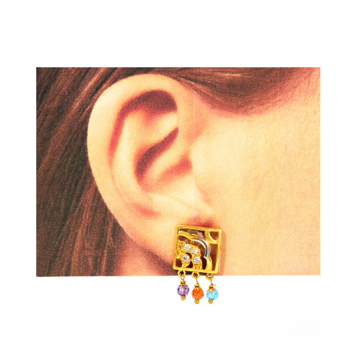 Gold earring with colorful drops worn by a person