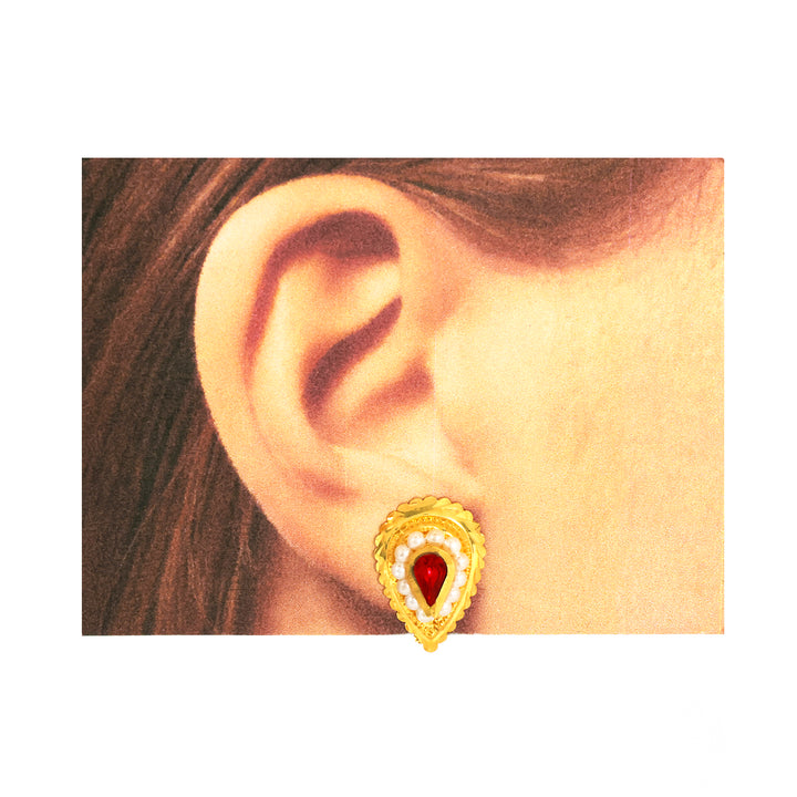 Gold earring with a red gemstone worn by a person