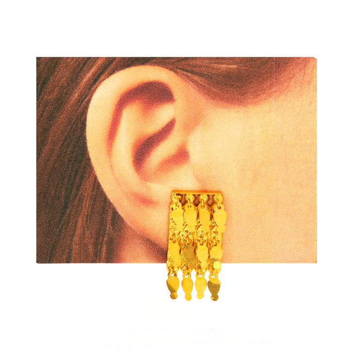 Gold earring worn on an ear with a neutral background