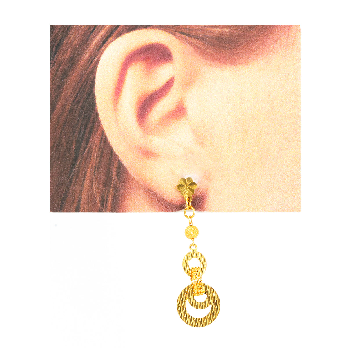 Gold earring worn on an ear with a plain background