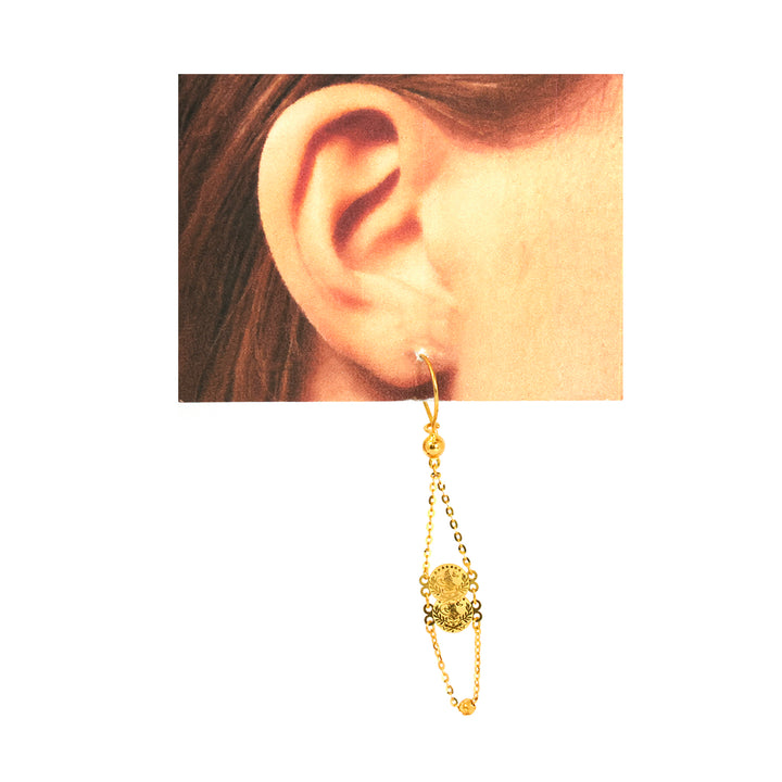 Gold earring worn on an ear with a plain background