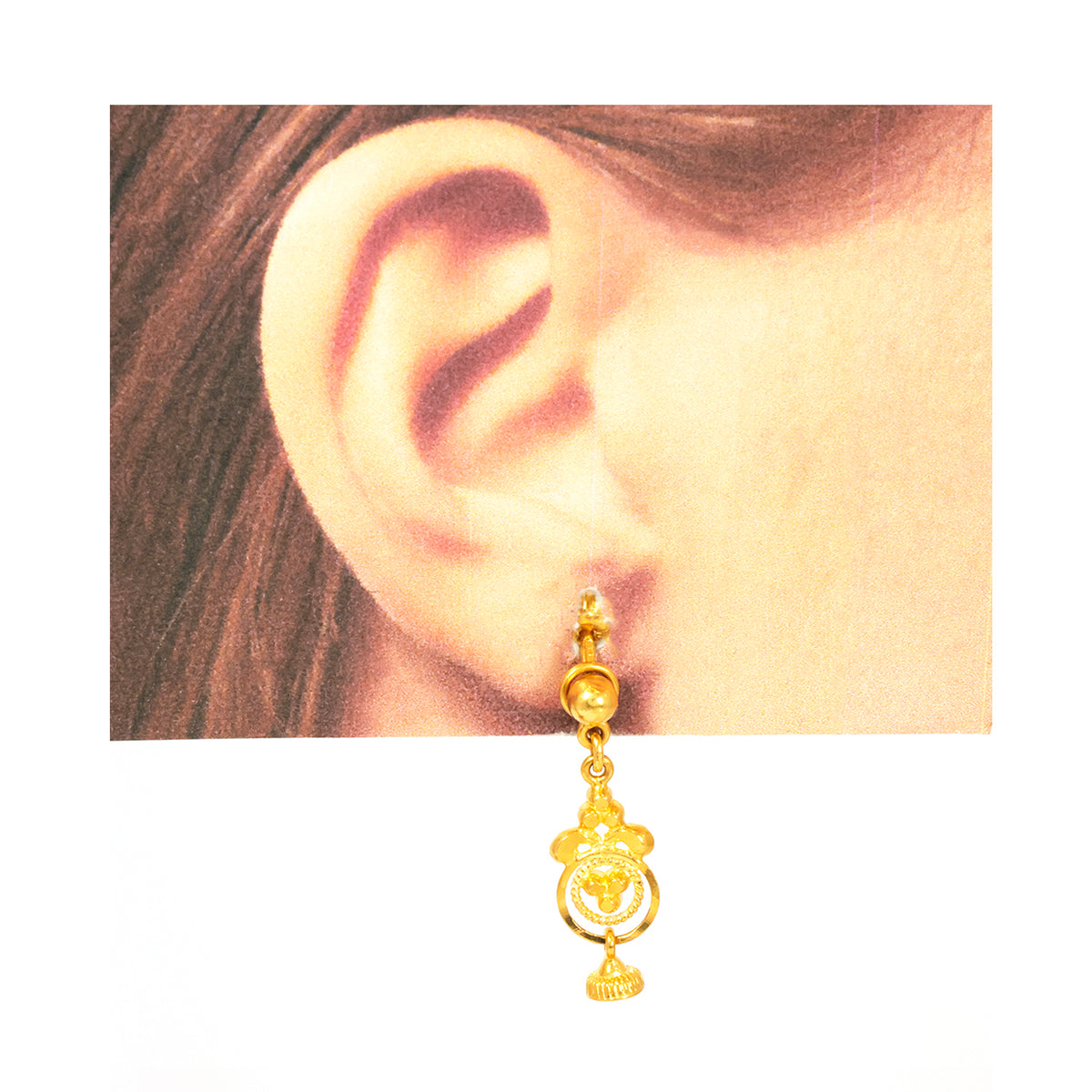 Gold earring worn on an ear with a plain background