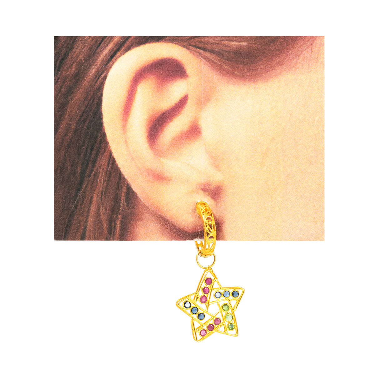 Gold star-shaped earring with colorful stones worn by a person.