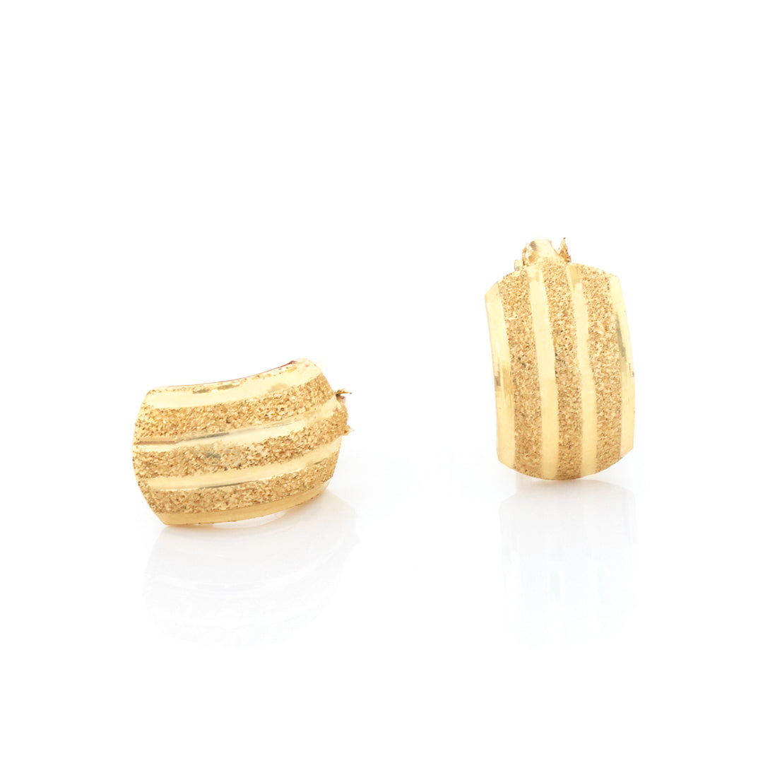 A pair of gold hoop earrings with a textured, striped hammered finish, displayed on a clean white reflective surface.