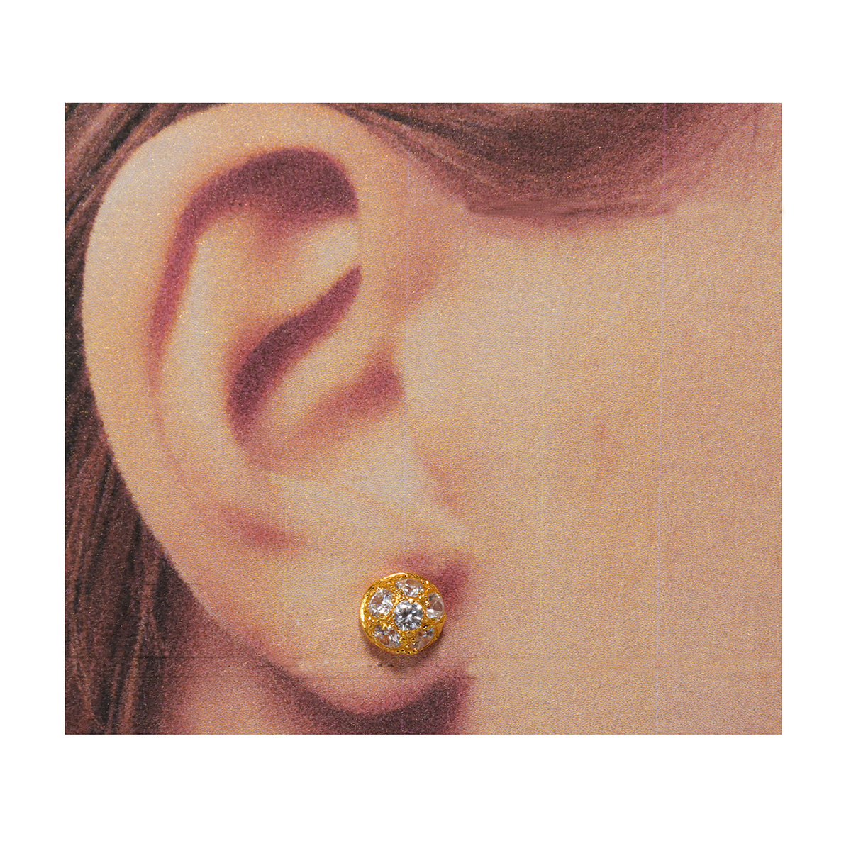 Gold earring with a clear gemstone worn on an ear