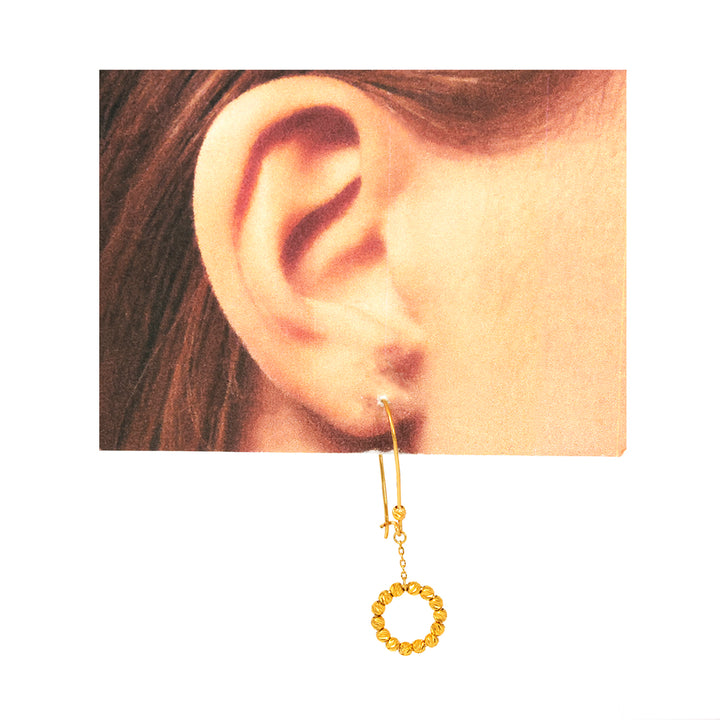 Gold hoop earring worn on a model's ear with a plain background