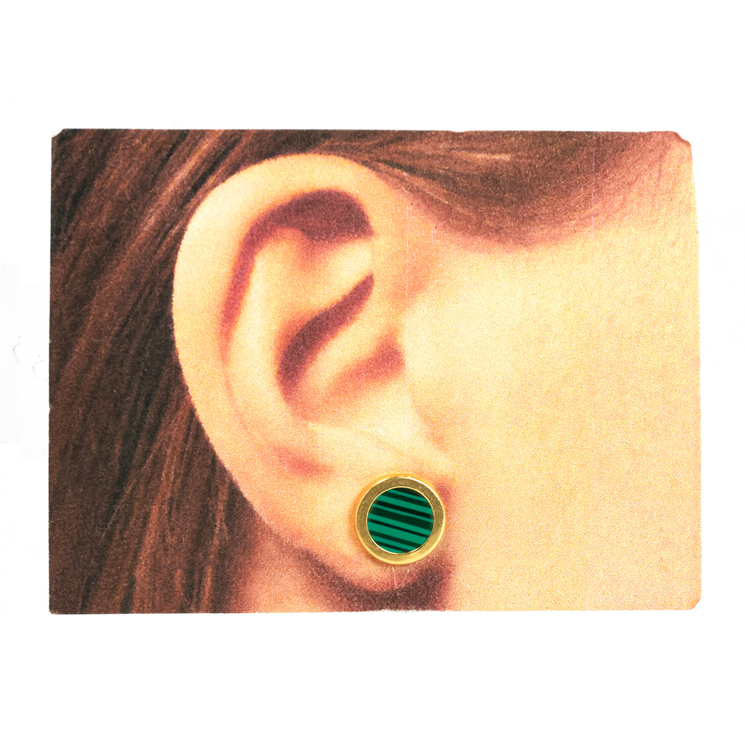 Close-up of an ear wearing a green and gold earring on a white background