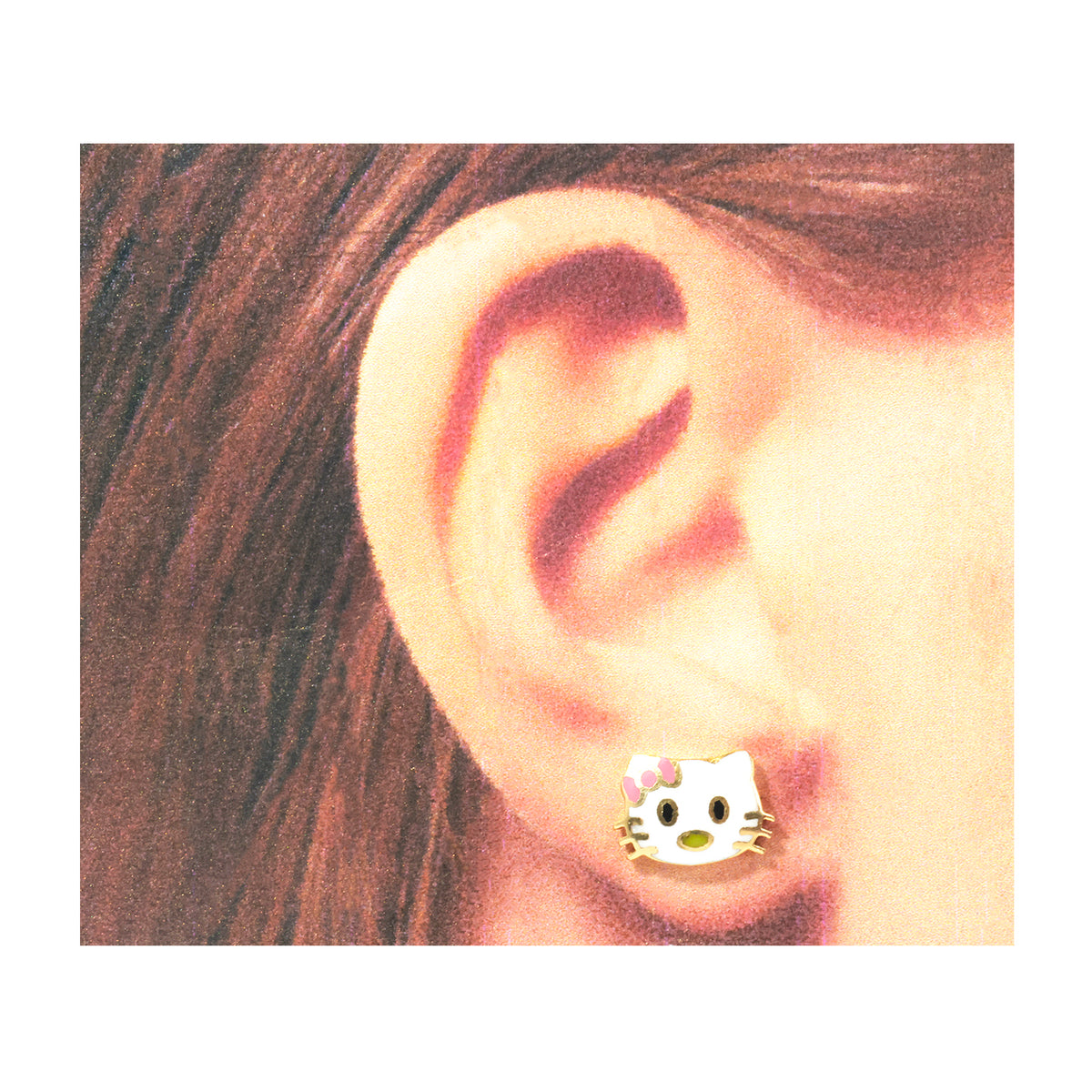 A close-up of a person's ear wearing a small Hello Kitty stud earring with a white face, black eyes and whiskers, and a pink bow.