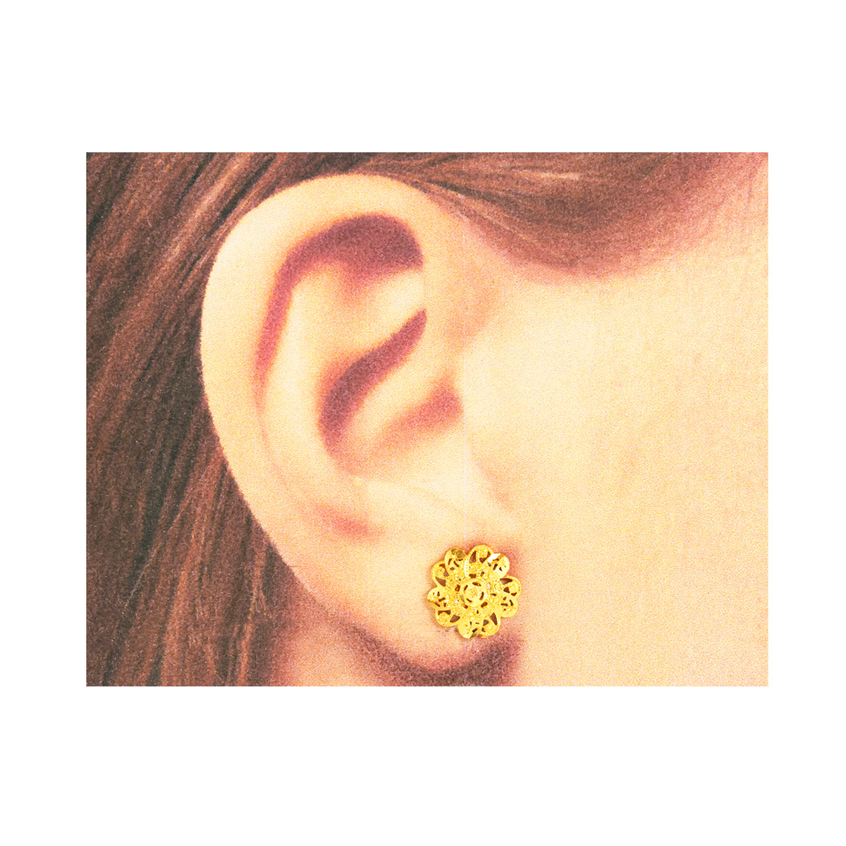 Gold floral earring worn on an ear with a plain background