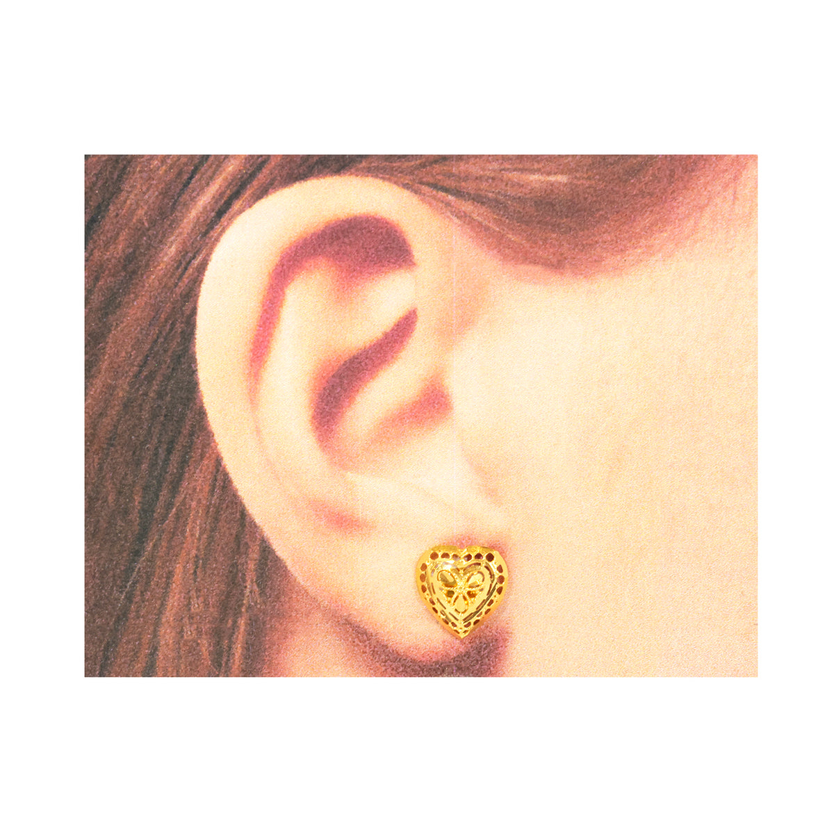 Gold heart-shaped earring worn on an ear with a plain background