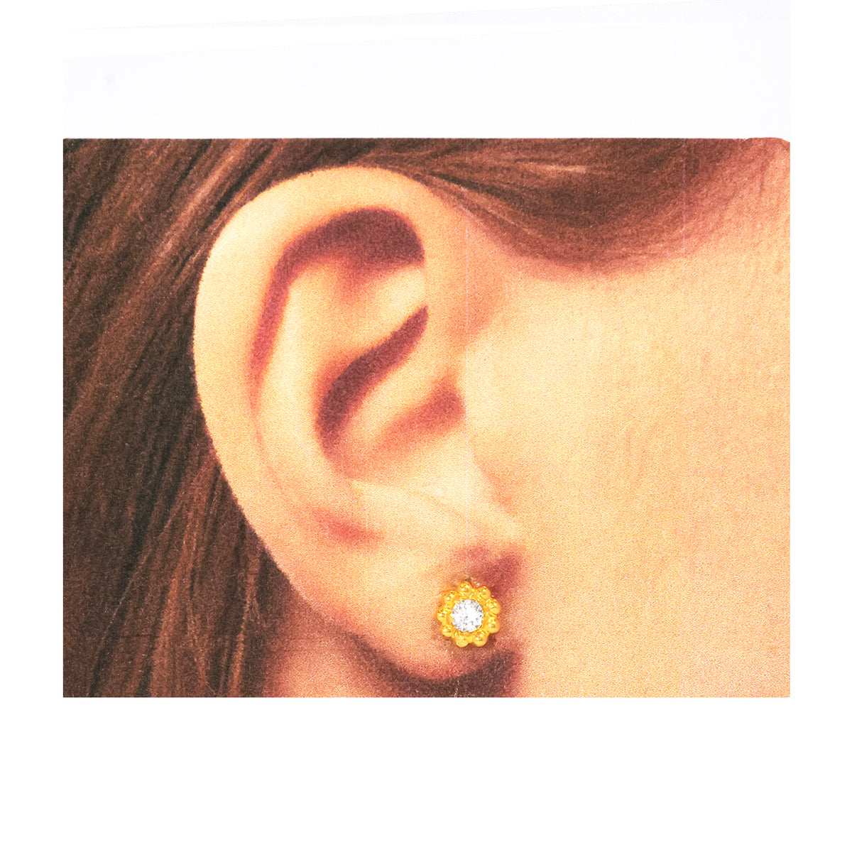 Close-up of an ear wearing a gold earring with a clear gemstone on a white background