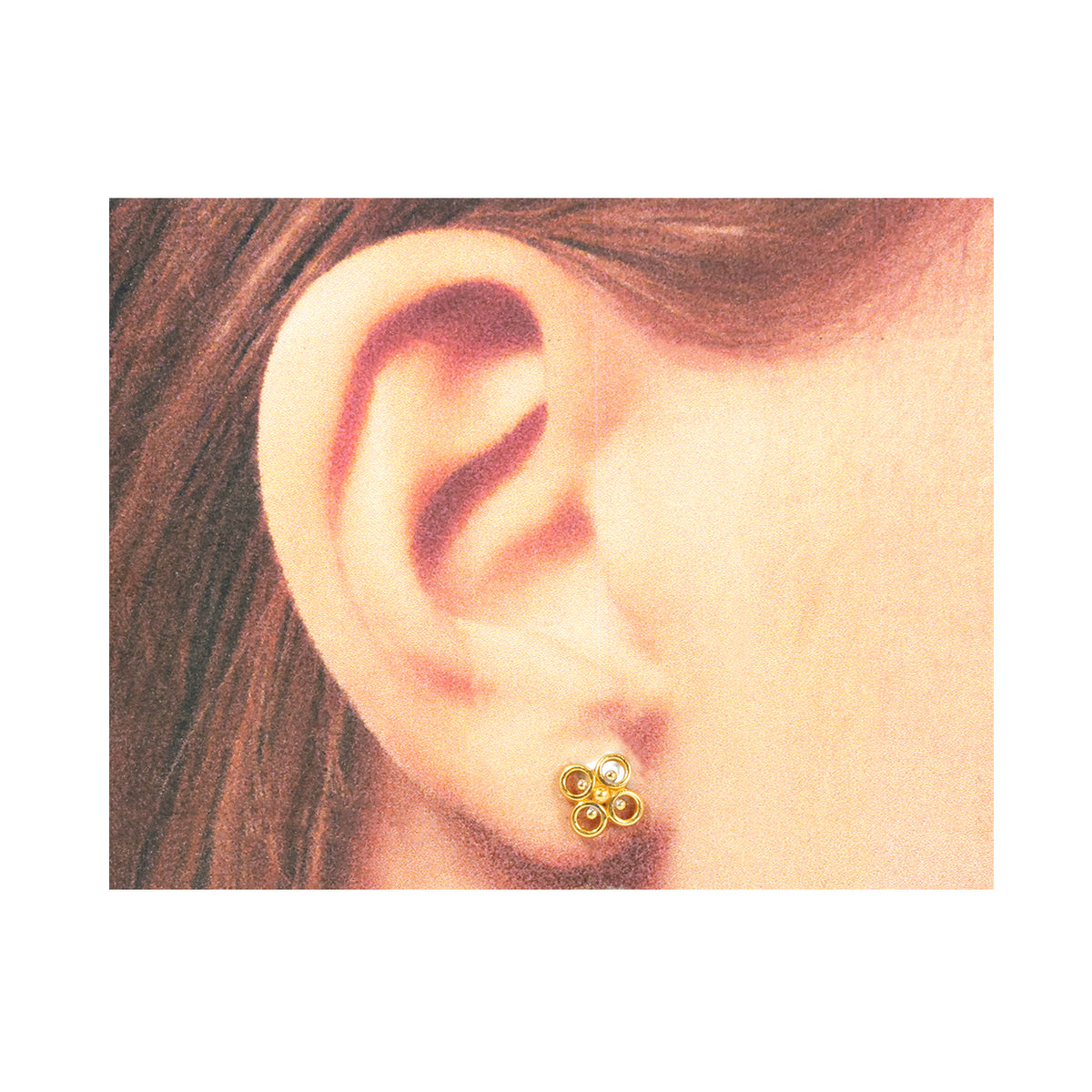 Close-up of an ear wearing a gold earring with three small round components.
