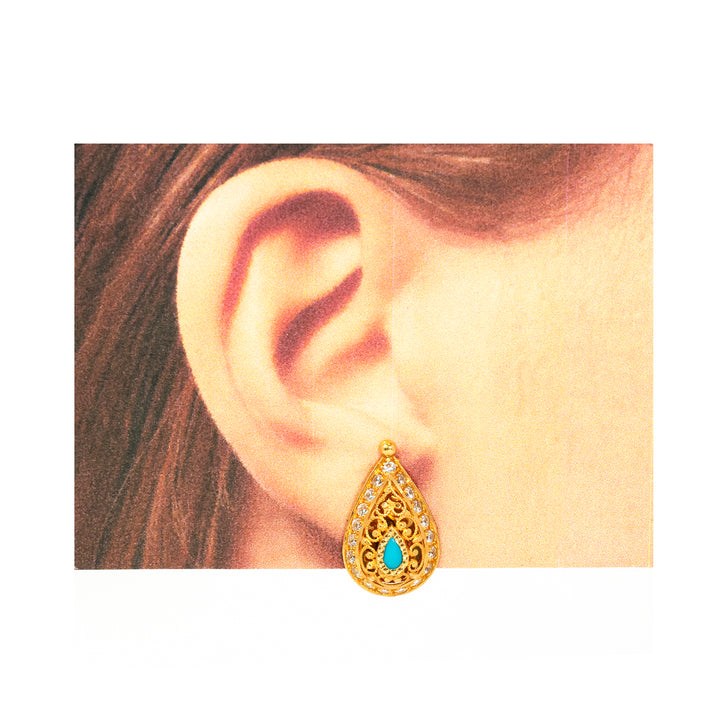 Gold earring with turquoise stone worn by a person