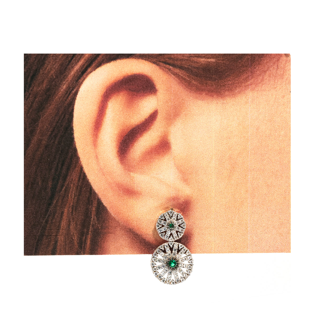 Close-up of an ear wearing a pair of silver earrings with green gemstones.