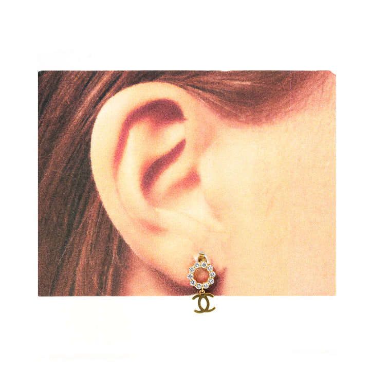 Close-up of an ear wearing a gold earring with a logo.