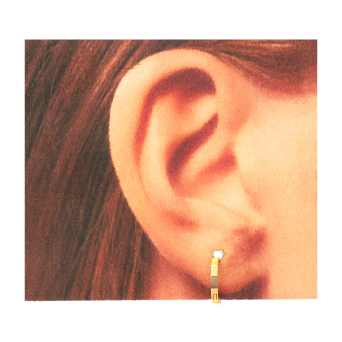 A close-up of a person's ear wearing a small gold hoop earring with a clear gemstone, shown against a warm-toned background.