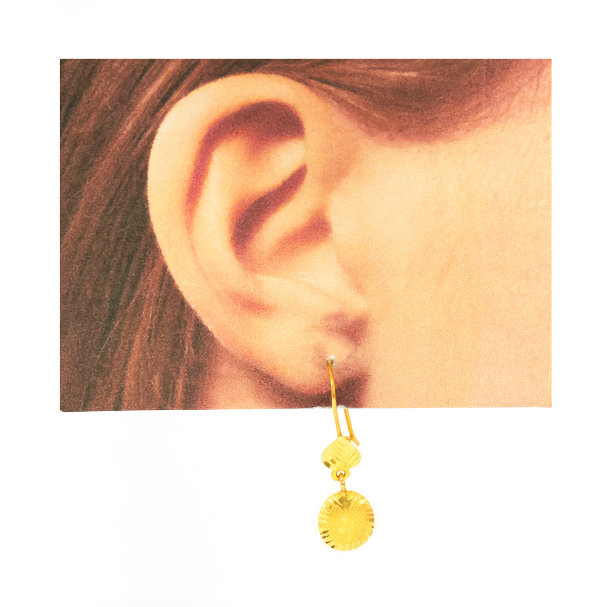 Gold earring worn on an ear with a plain background