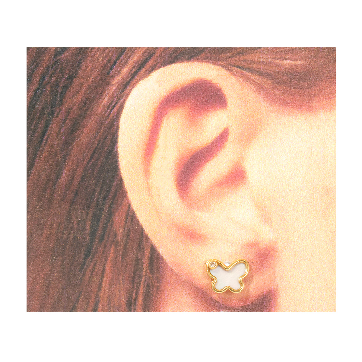 A close-up of a person's ear wearing a small butterfly-shaped stud earring with a gold outline and white center, set against a white border.